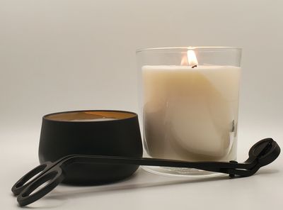 Two candles and a wick trimmer on a white background.