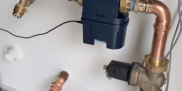 Copper and brass plumbing pipes with a blue valve mounted on a white wall.