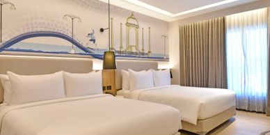 Modern hotel room with two neatly made beds and cityscape wall art.