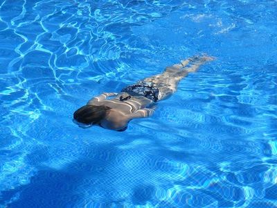 Person swimming underwater in a clear blue pool.