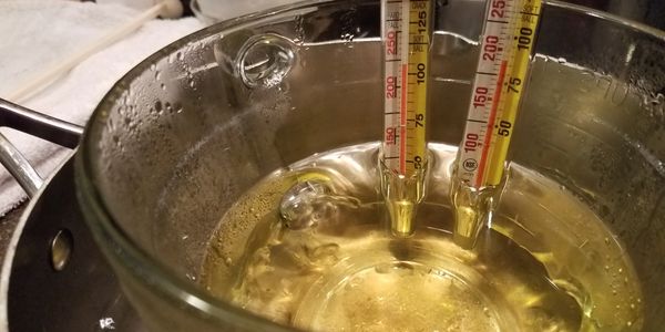 Two candy thermometers submerged in a glass bowl of liquid.
