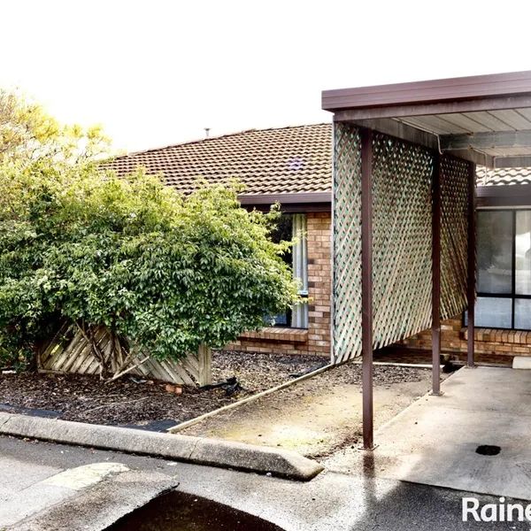 Carport and greenery in front of a brick house under a tiled roof.