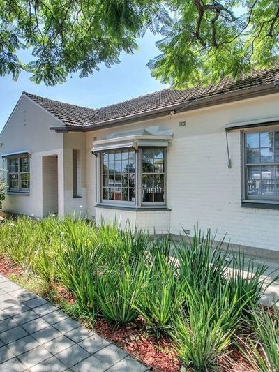 Cozy white brick house with a tiled roof and a paved walkway surrounded by greenery.