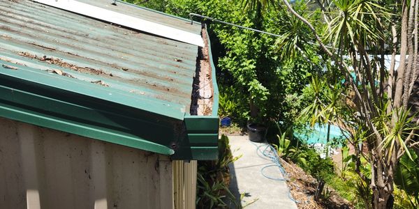 View of a green metal roof with surrounding garden and pool area.