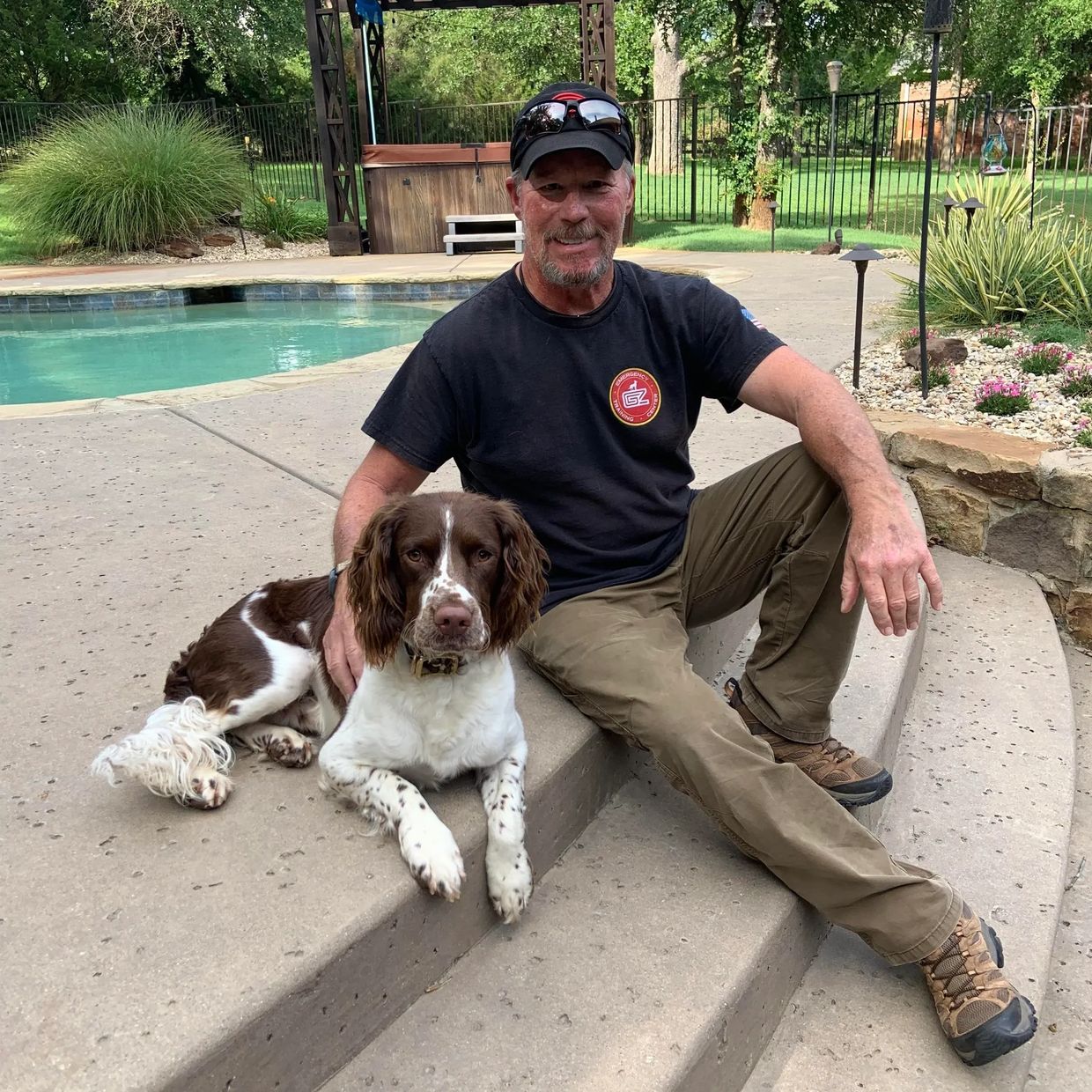 Man sitting on steps with a brown and white dog beside a pool.