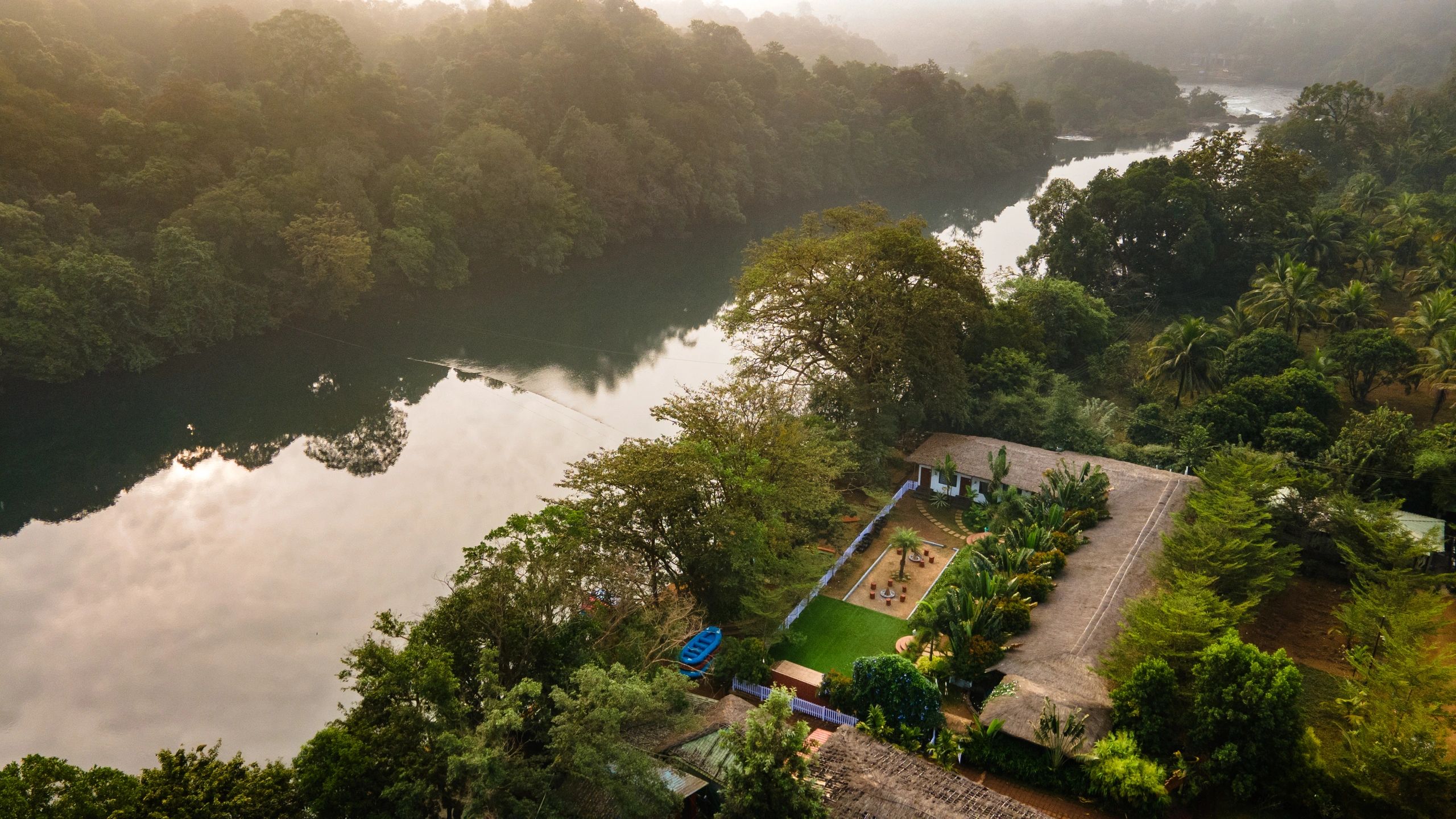 Serene river winding through lush green forest with a cozy house nearby.
