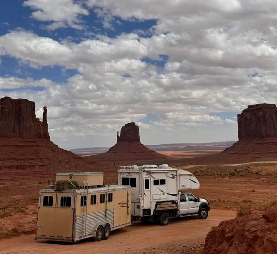 Truck camper pulling a 4 horse trailer past the iconic mittens in Monument Valley Utah.