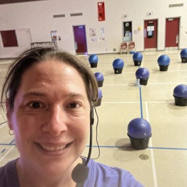 Smiling woman with headset in a gym with spaced blue exercise balls.