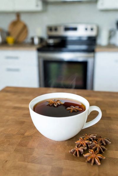 A white cup of tea with star anise on a wooden table.