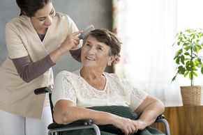 Caregiver gently combs elderly woman's hair in a wheelchair.