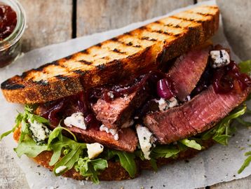 Grilled steak sandwich with arugula and blue cheese on toasted bread.