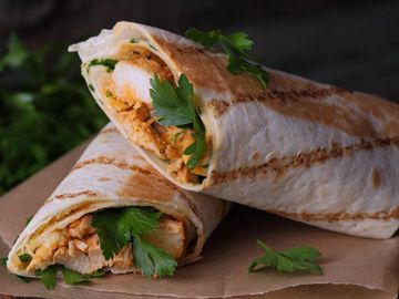 Two grilled chicken wraps garnished with fresh parsley on brown paper.