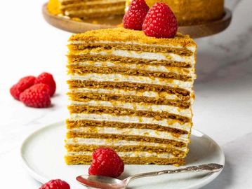 Slice of layered honey cake topped with fresh raspberries.