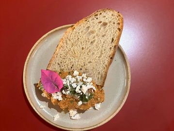 Slice of bread with a spread topped with cheese and a purple leaf on a beige plate.