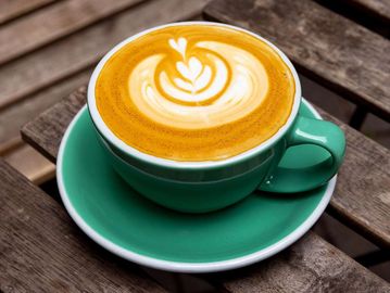 A green cup of latte with heart-shaped latte art on a wooden table.