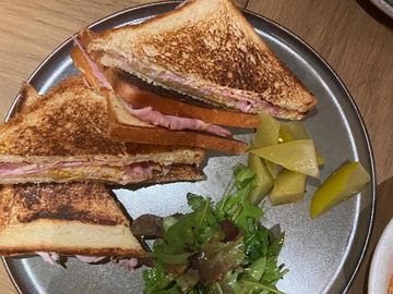 Grilled ham and cheese sandwich with pickles and fresh greens.