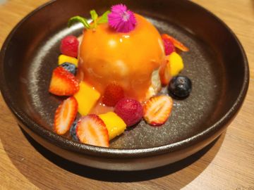 Colorful dessert topped with orange sauce and fresh berries in a black bowl.