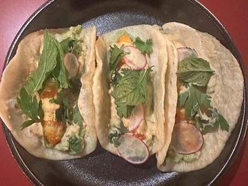 Three soft tacos filled with vegetables and herbs on a black plate.