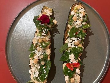 Two elegant toasted bread slices topped with herbs, cheese, and chickpeas on a gray plate.