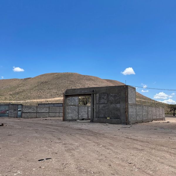Partially constructed concrete block walls in a dry, open area with a hill and clear blue sky.