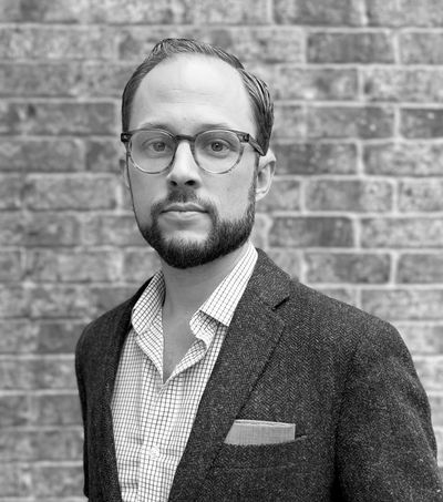 Portrait of a man with glasses in front of a brick wall.