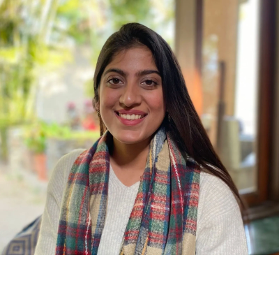 Smiling woman in a white sweater and colorful scarf indoors with natural light.