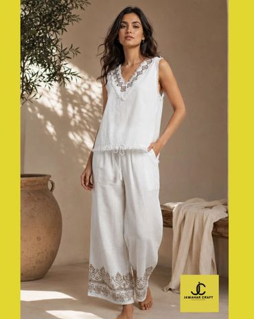 Woman in white sleeveless top and wide-leg pants with embroidery.
