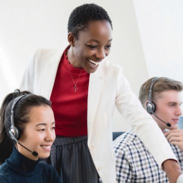 A professional woman assists two headset-wearing call center agents.