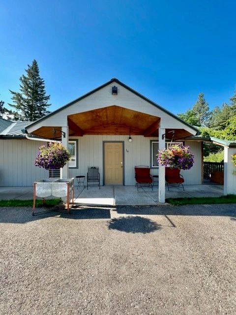 Cozy house entrance with hanging flower baskets and outdoor seating under a wooden porch roof.