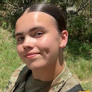 Young woman in military uniform smiling outdoors.
