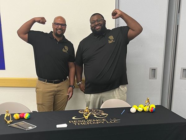Two men flexing at a Resilience Therapy LLC booth.