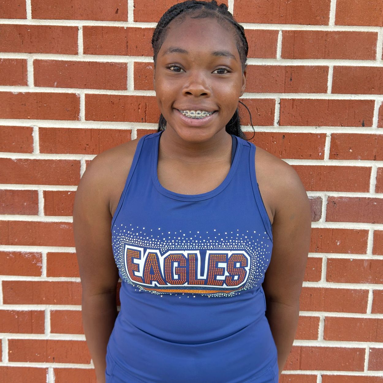 Smiling girl in blue Eagles tank top standing against a brick wall.