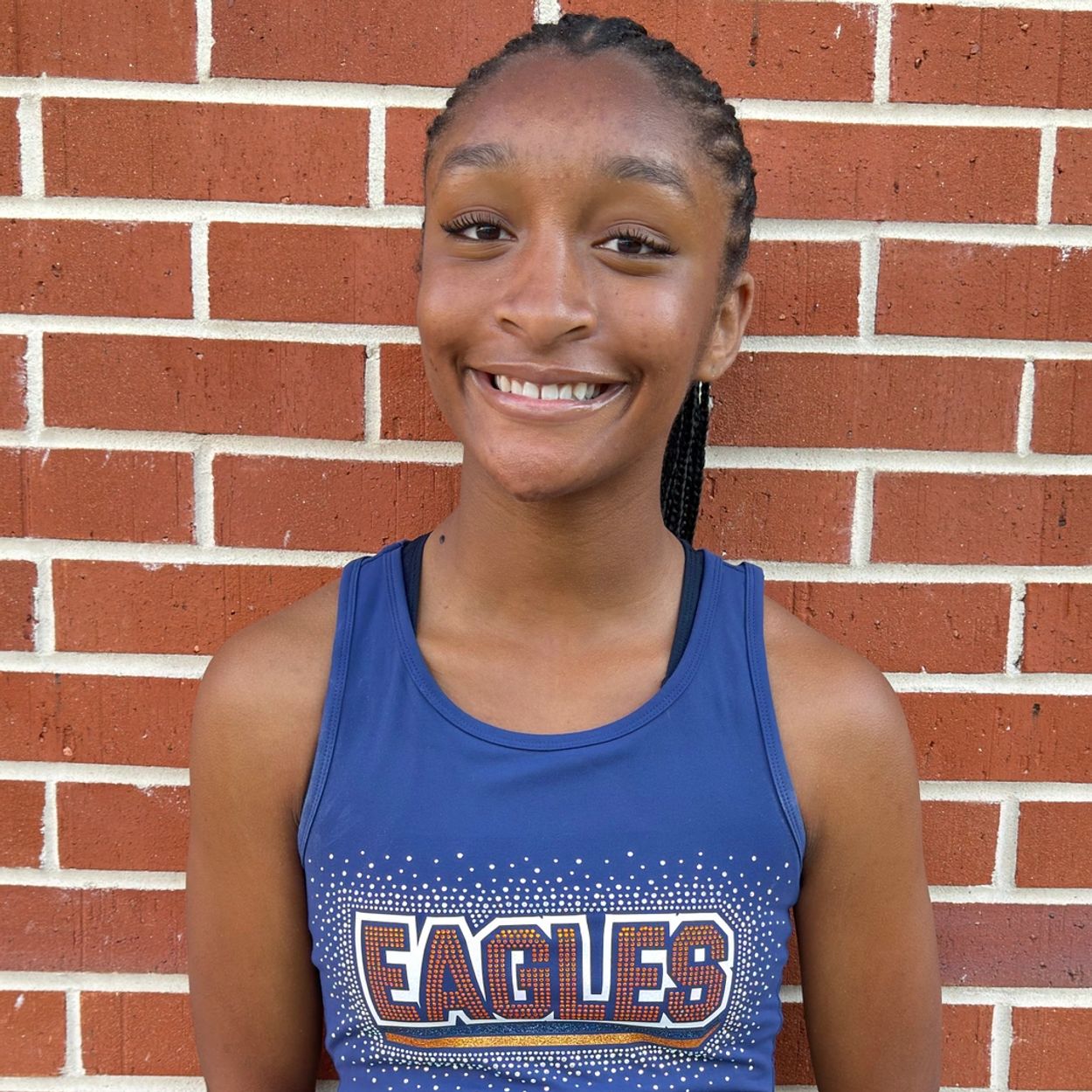 Smiling young athlete in blue Eagles tank top against brick wall.