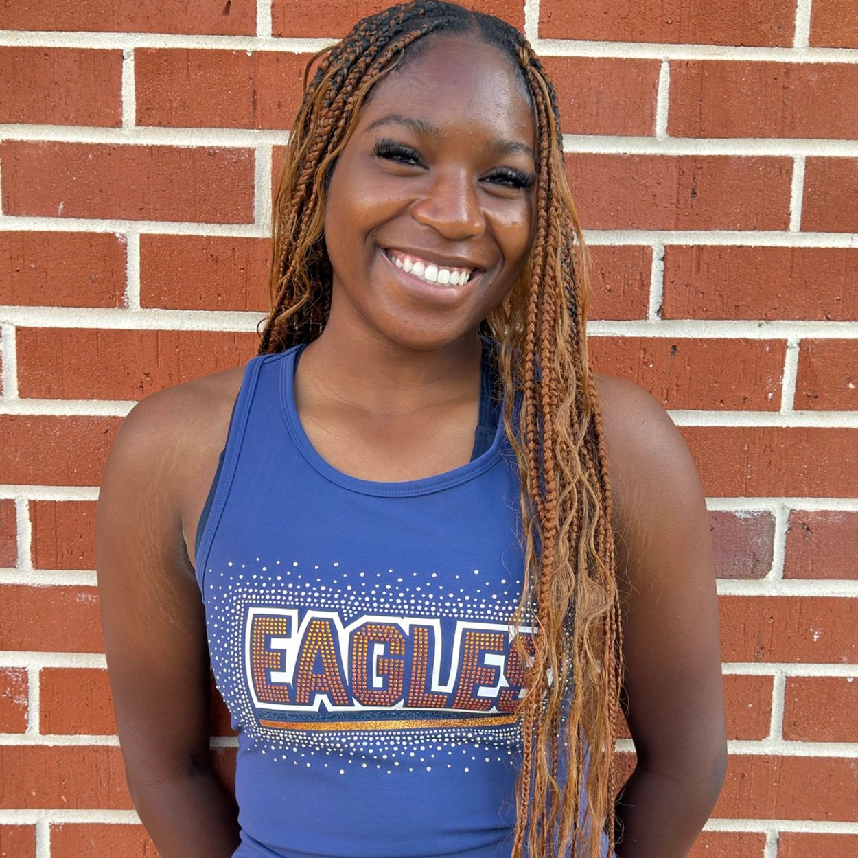 Smiling woman in a blue Eagles tank top stands against a brick wall.