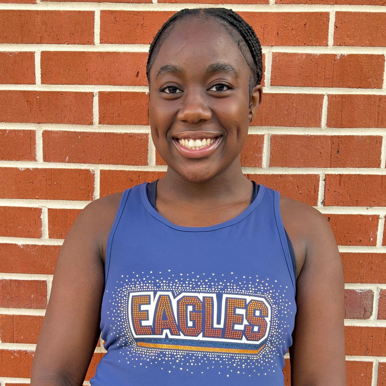 Smiling young woman in a blue Eagles sports top stands against a brick wall.