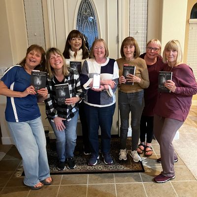 Group of women holding books, smiling inside a home.