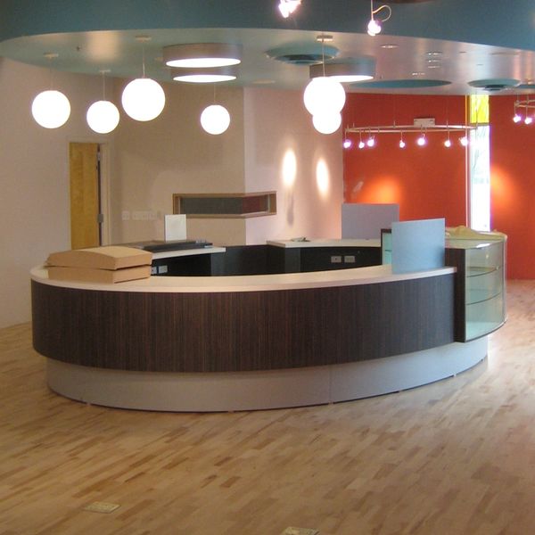 Modern curved reception desk in a spacious office lobby with hanging globe lights.