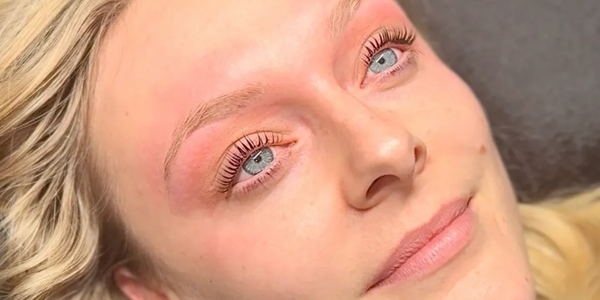 Close-up of a woman with light blonde hair and blue eyes lying on a dark surface.