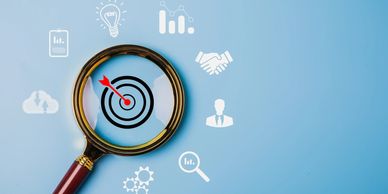 Magnifying glass focusing on a target with business icons around it.