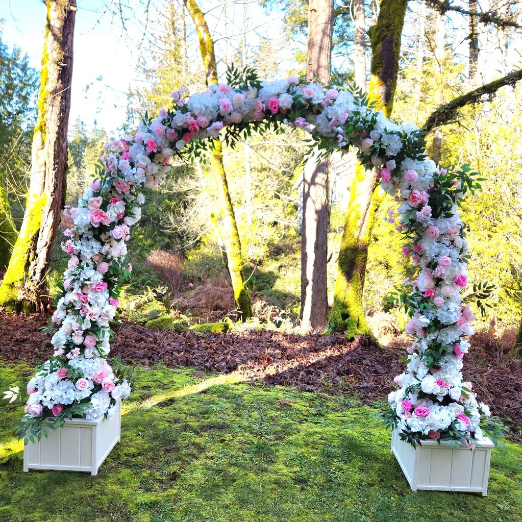 Floral arch with pink and white flowers in a forest setting.