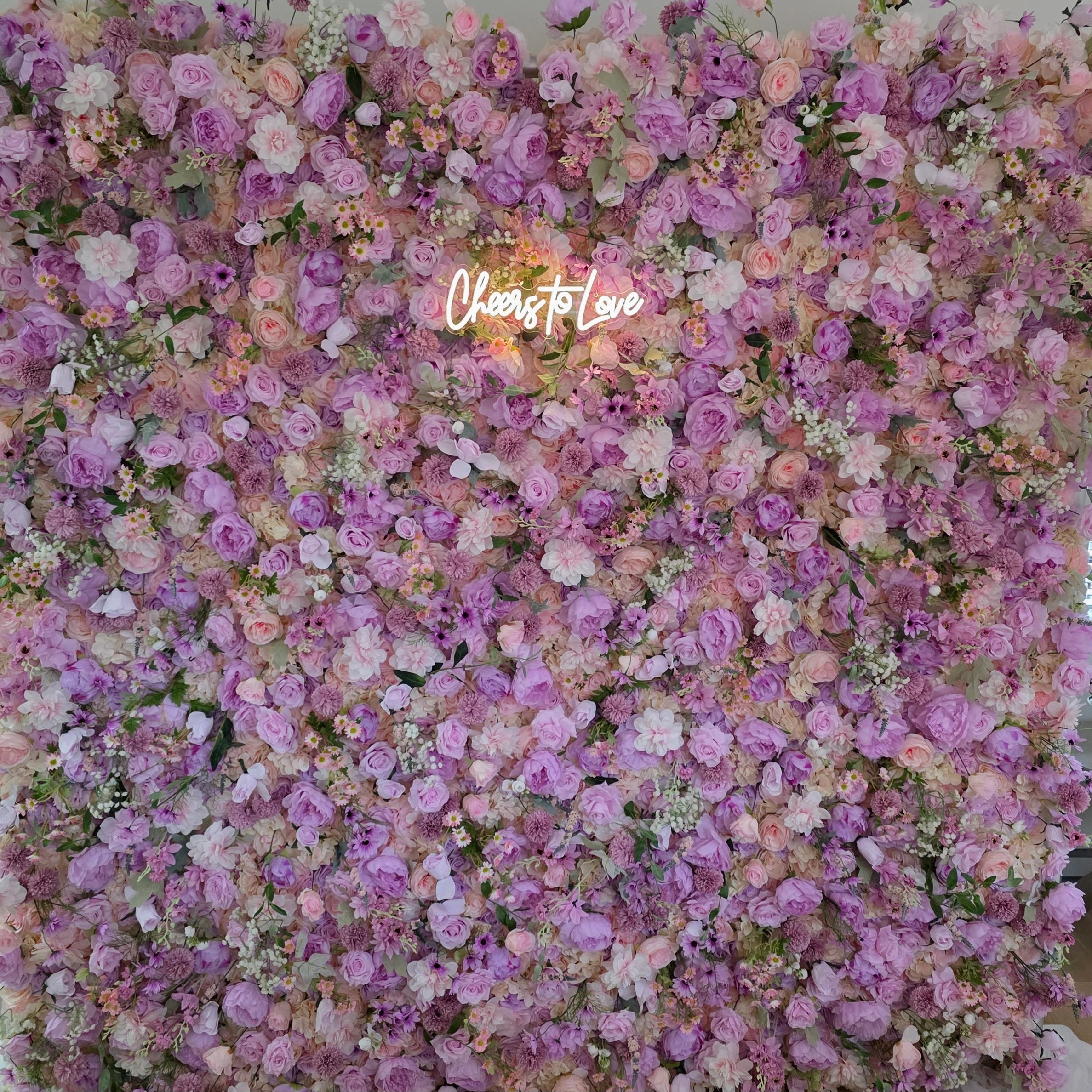A vibrant floral wall with pink and purple flowers and a 'Cheers to Love' neon sign.