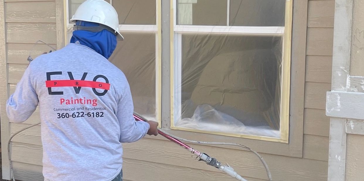 A painter spray-painting the exterior of a house under construction.