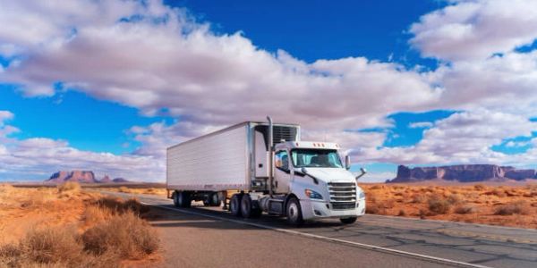 White semi-truck driving on highway through desert landscape.