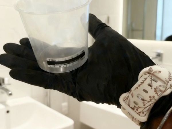 Hand wearing black glove holding a clear plastic measuring cup.