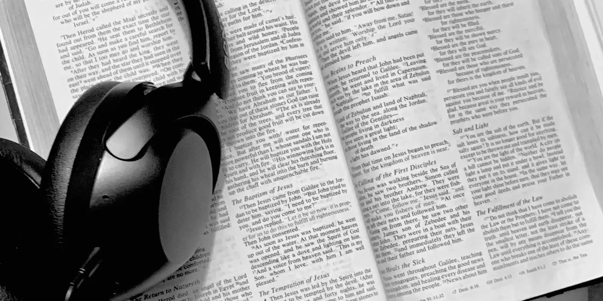 Headphones rest on an open Bible showing the Book of Matthew.