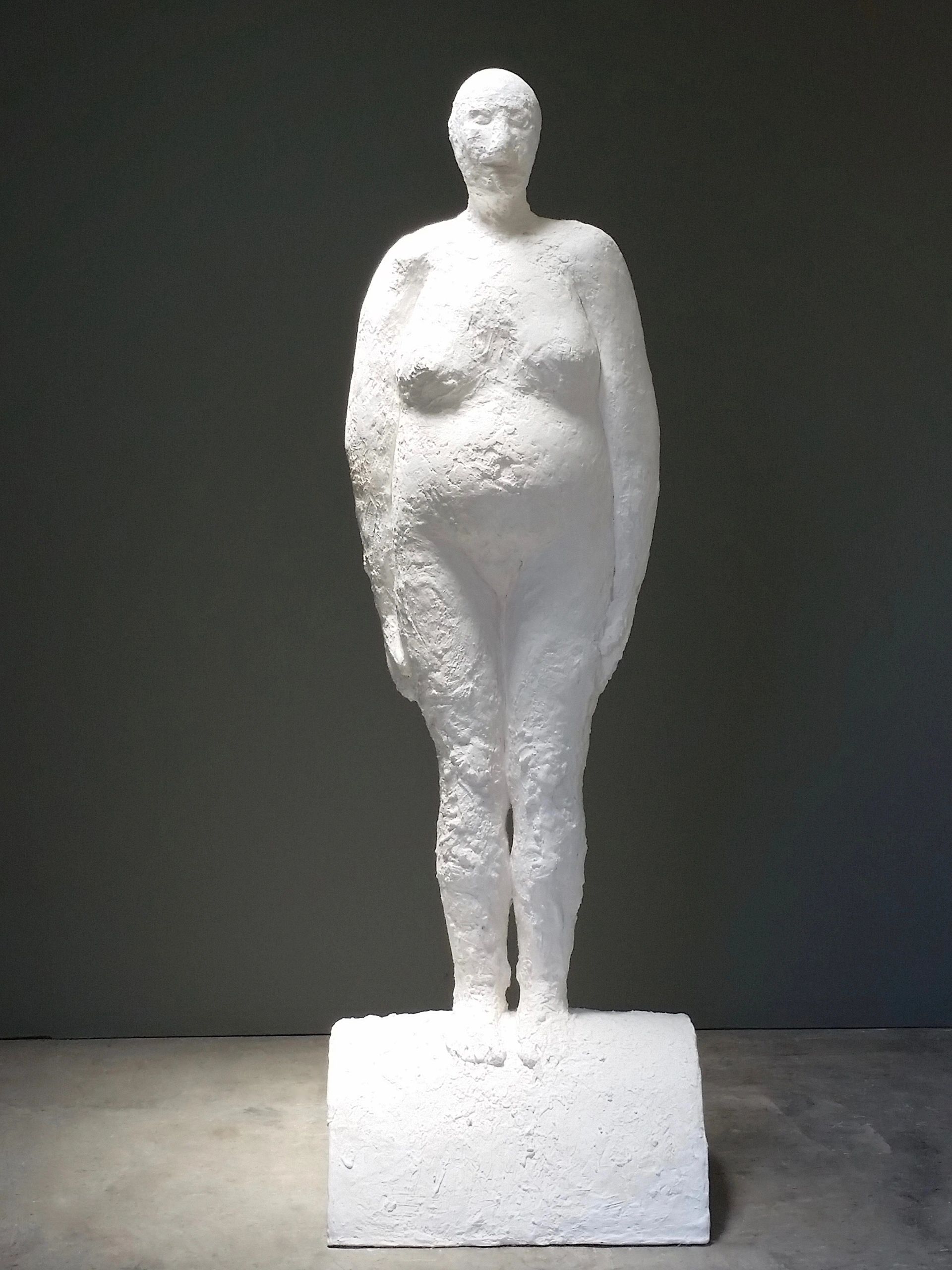 Rough-textured white sculpture of a standing human figure on a rectangular base.