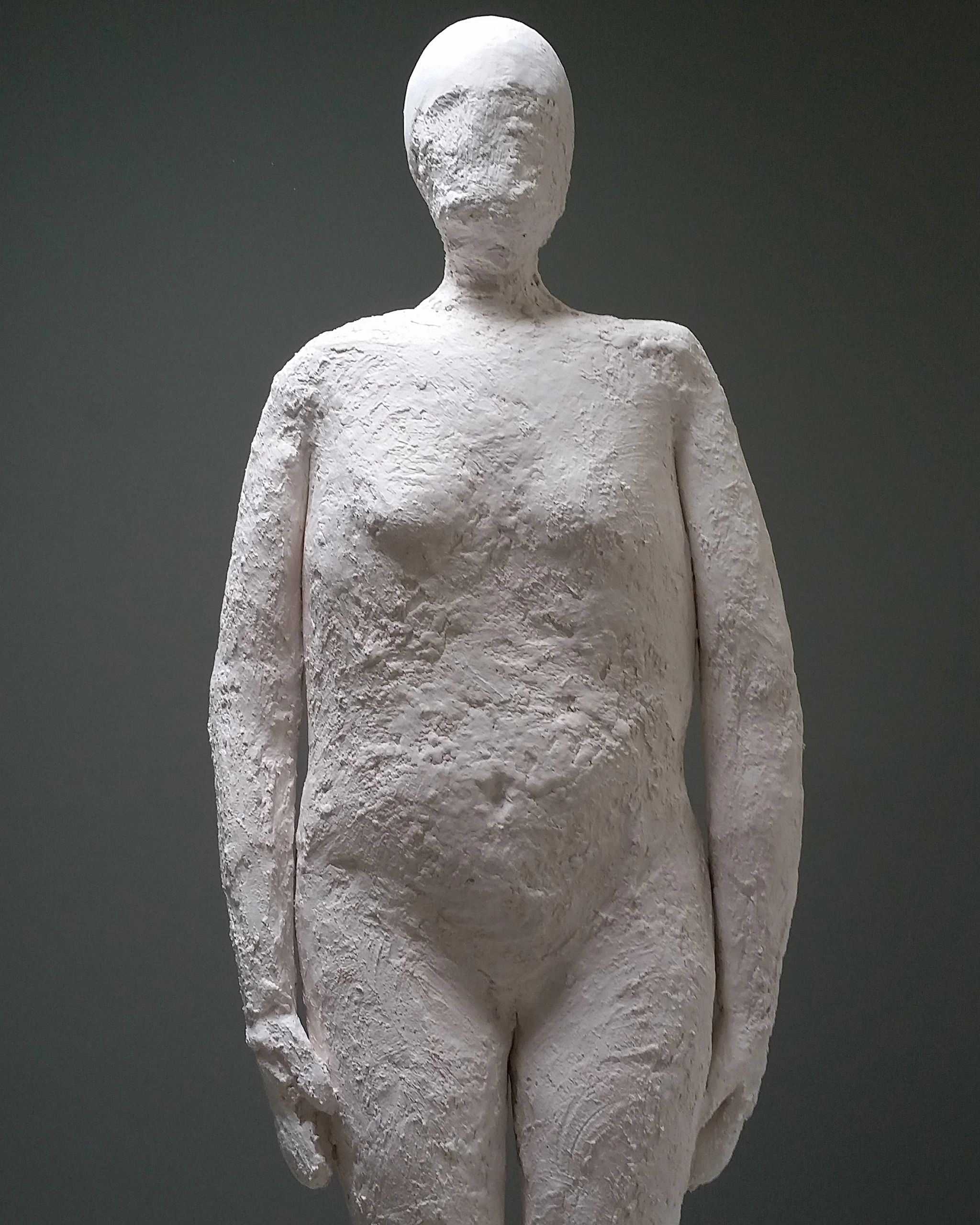 A rough-textured, faceless white sculpture of a human figure.