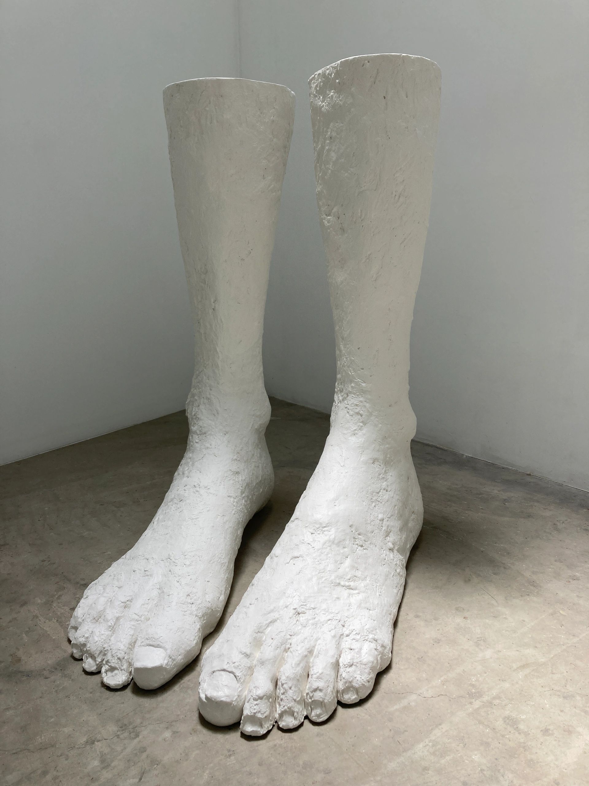 Giant white sculpted feet and lower legs in a minimalist room.