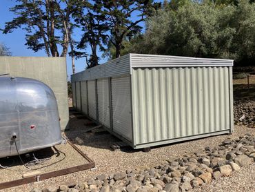 Metal storage containers outdoors surrounded by rocks and trees.