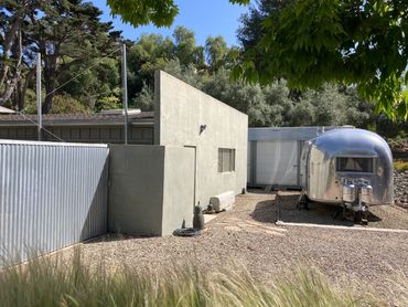 Modern small concrete building beside a silver trailer in a sunlit outdoor setting.